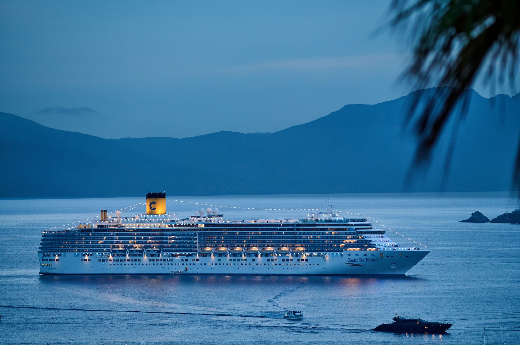 Cruise ship arriving at a Mediterranean harbor at dusk, mountains in the distance